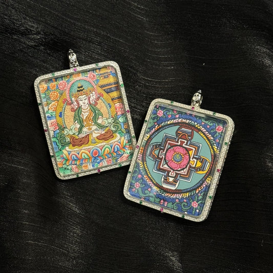 Front and back view of a Vairocana Buddha mini thangka pendant showing the hand-painted Vairocana seated on a lotus throne and a sacred mandala design on the reverse side, enclosed in a square 925 sterling silver pendant case with gemstone accents.