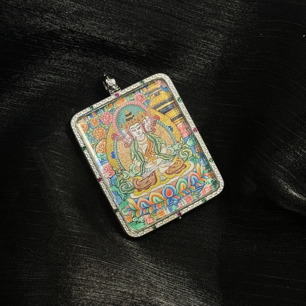 Front view of the Vairocana Buddha mini thangka pendant showing the Buddha seated in meditation posture on a multicolored lotus base with detailed Tibetan floral background and ornate halo.