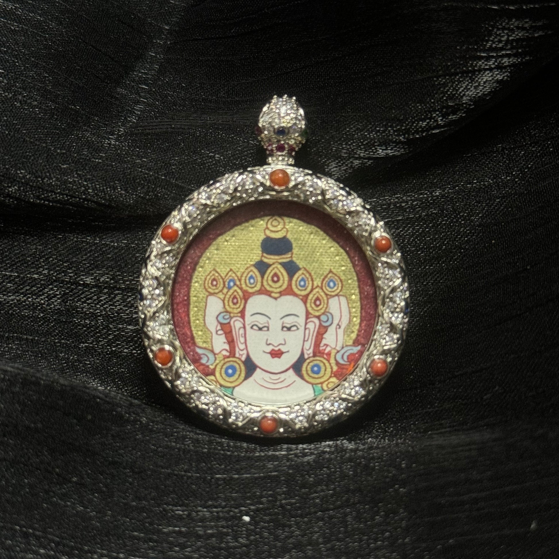 Close-up of Vairocana Buddha miniature thangka pendant showing hand-painted red gold Buddha head with cinnabar mineral pigment background and ornate jeweled copper pendant frame