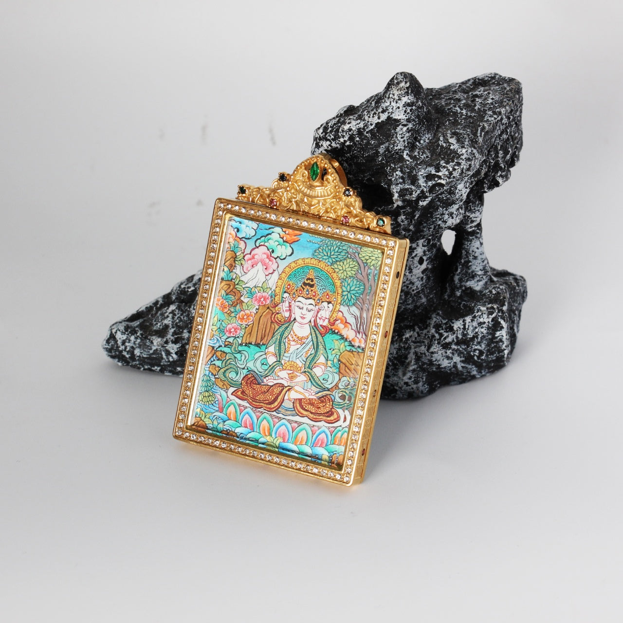 Perspective view of a Vairocana Buddha mini thangka pendant showing the gold-tone jewelry case, crystal border, and detailed hand-painted Buddhist artwork in Nepal colored thangka style