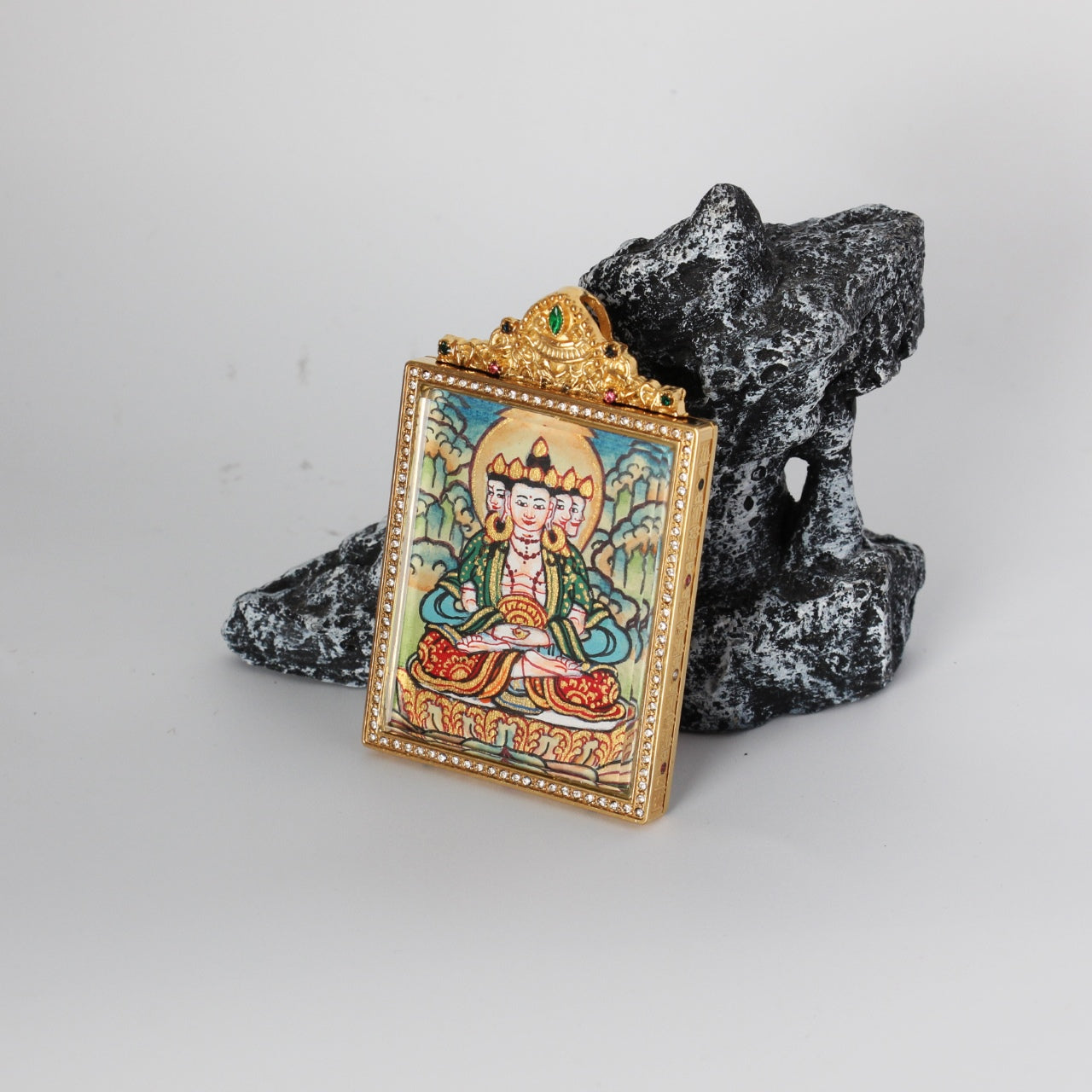 Side-angled photo of Vairocana Buddha mini thangka pendant showing the gold-tone titanium steel case profile, crystal border around the front window, and the hand-painted Vairocana Buddha image inside.