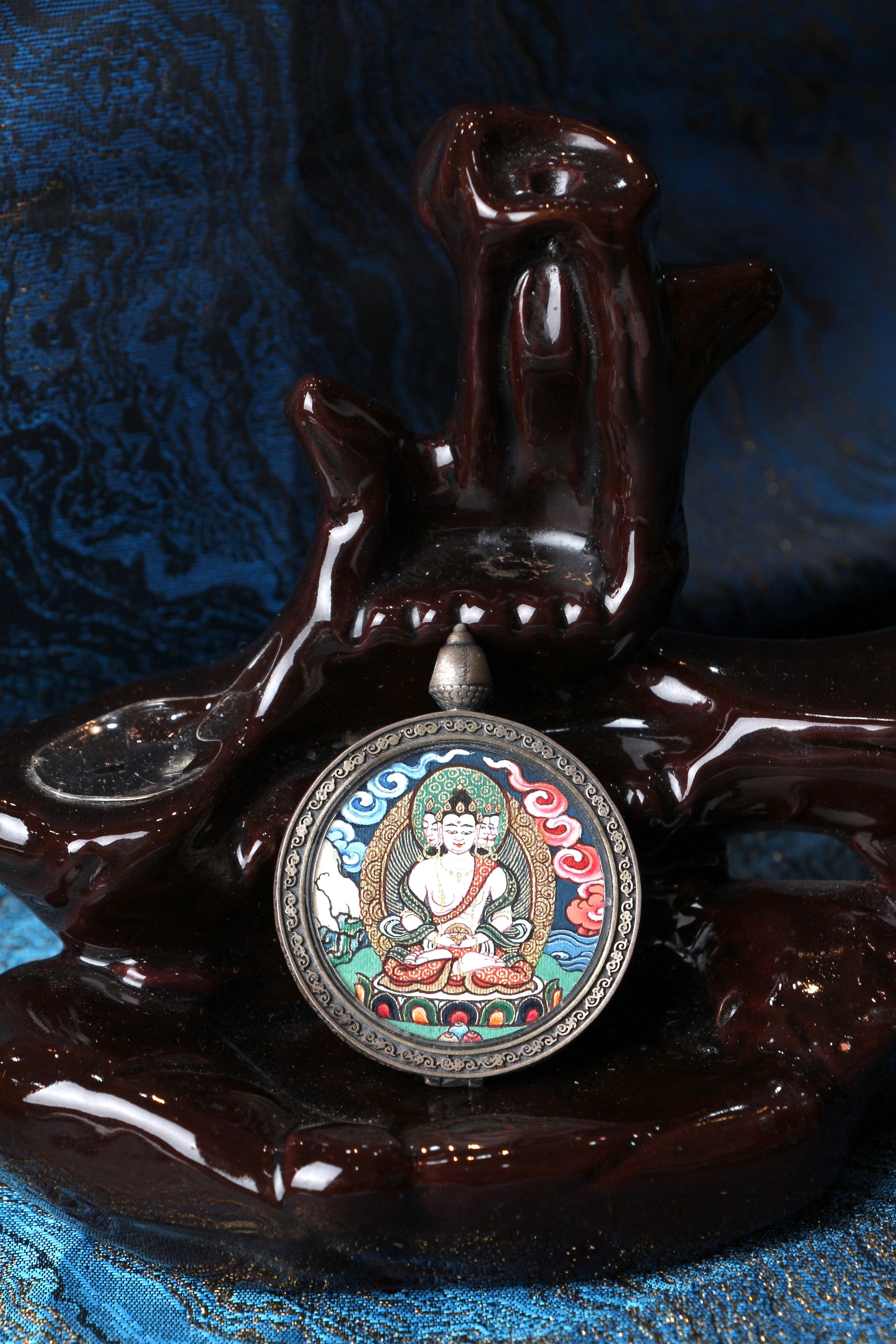 Front view of a circular Vairocana Buddha thangka pendant, fully hand-painted in the Rebgong cloud-background style with mineral pigments, set in a 925 silver frame, miniature Buddhist devotional artwork.