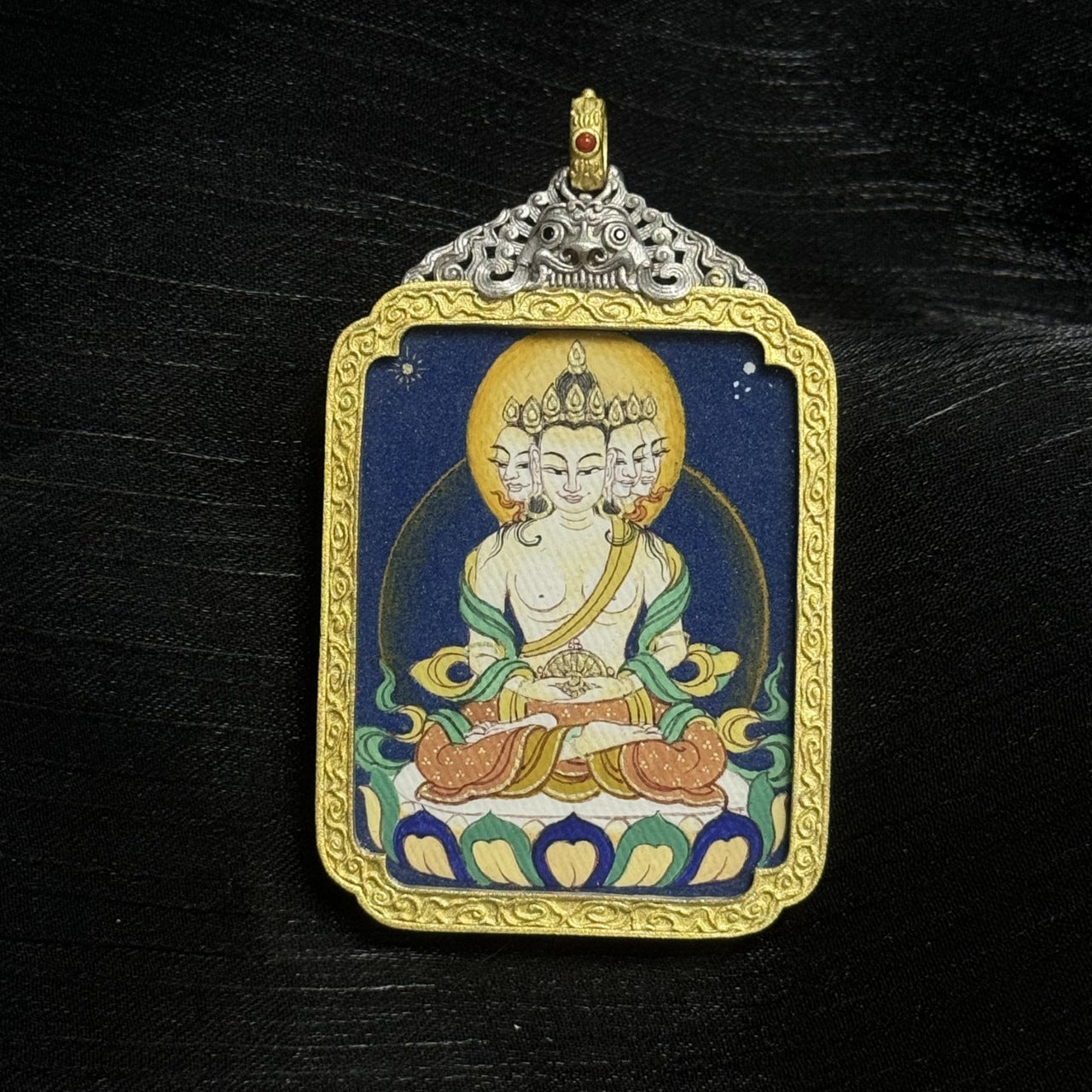 Detail of the electroplated silver case and bail of a Vairocana Buddha mini thangka pendant, showing traditional Tibetan decorative metalwork.
