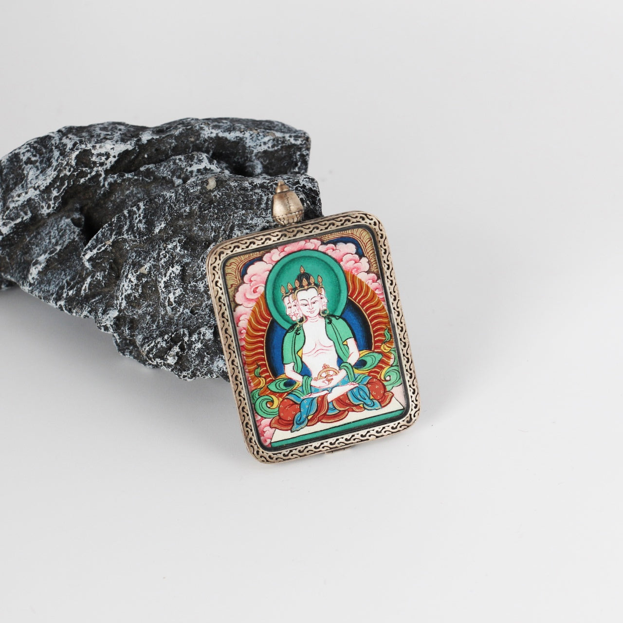 Vairocana mini Thangka pendant displayed on a stone prop, emphasizing the vivid hand-painted artwork, green-blue halo tones, and the detailed engraved pure silver frame.