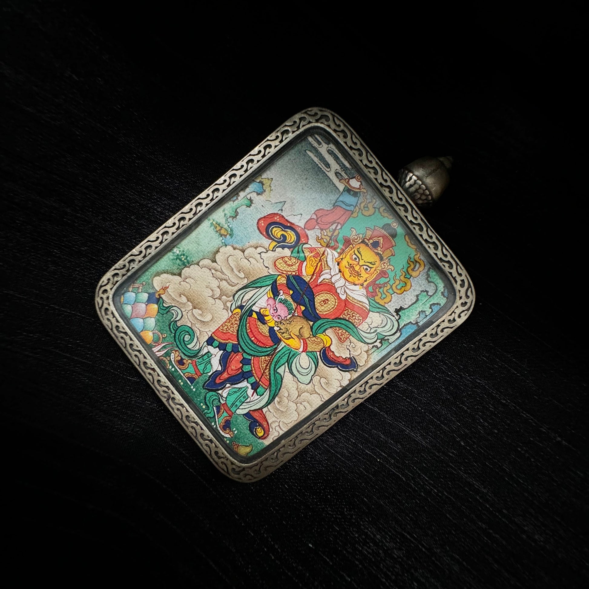 Vaishravana Northern Guardian King mini thangka pendant displayed on dark fabric background highlighting Tibetan hand-painted protector deity artwork