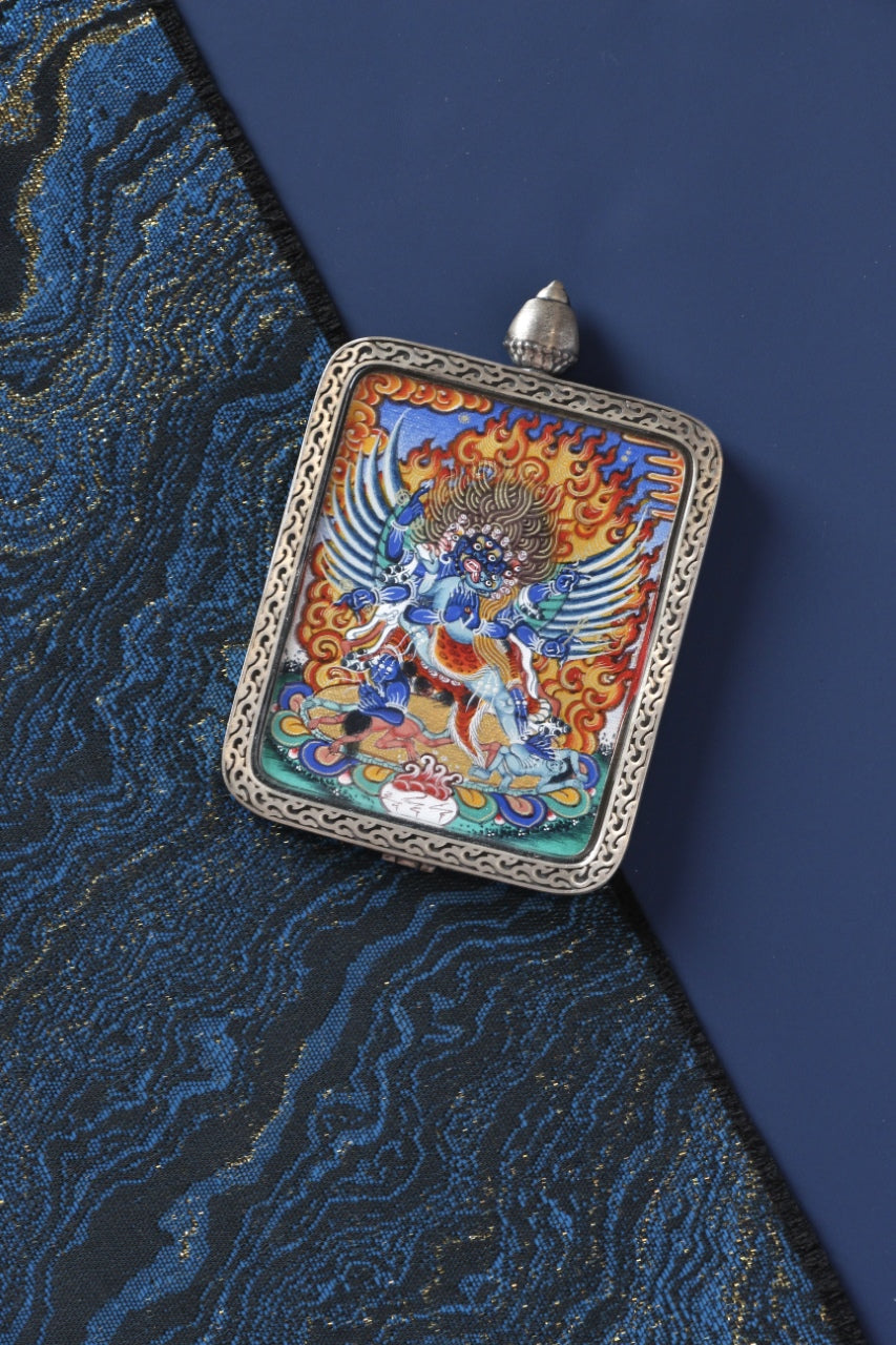 Angled view of a Vajrakilaya mini thangka pendant in a sterling silver style case, presented as a portable Tibetan Buddhist art piece suitable for collectors and personal shrine display.