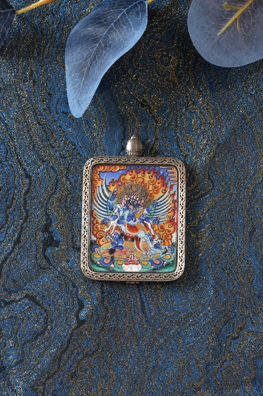 Flat lay of a Vajrakilaya (Dorje Phurba) mini thangka pendant highlighting detailed hand-painted iconography, mineral pigment coloration, and the protective silver pendant frame.