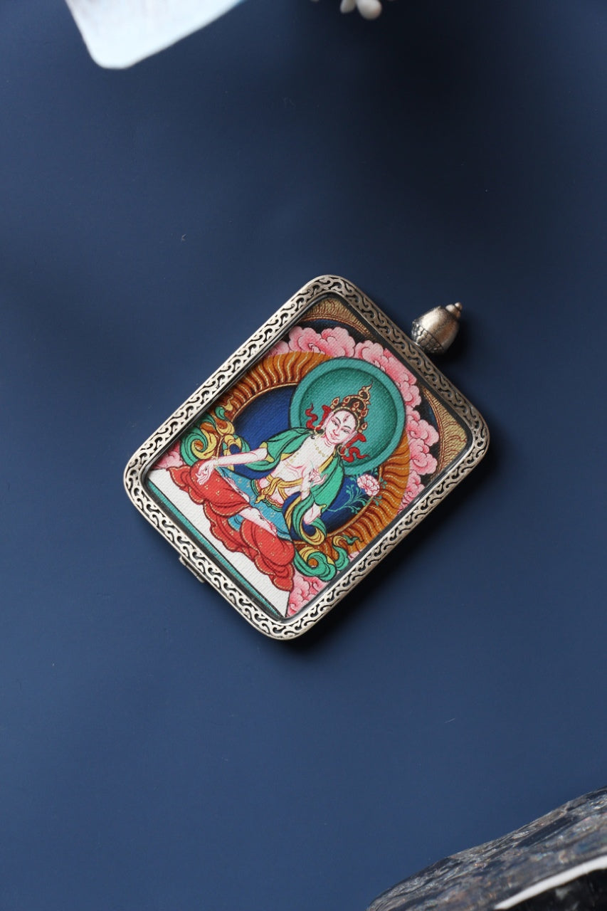 Angled product view of the White Tara mini thangka pendant from the Tibetan Red Cloud Zangka Series, fully hand-painted with natural mineral pigments and presented in a Dunhuang Nine-Colored Deer sterling silver case for portable devotion and collecting.