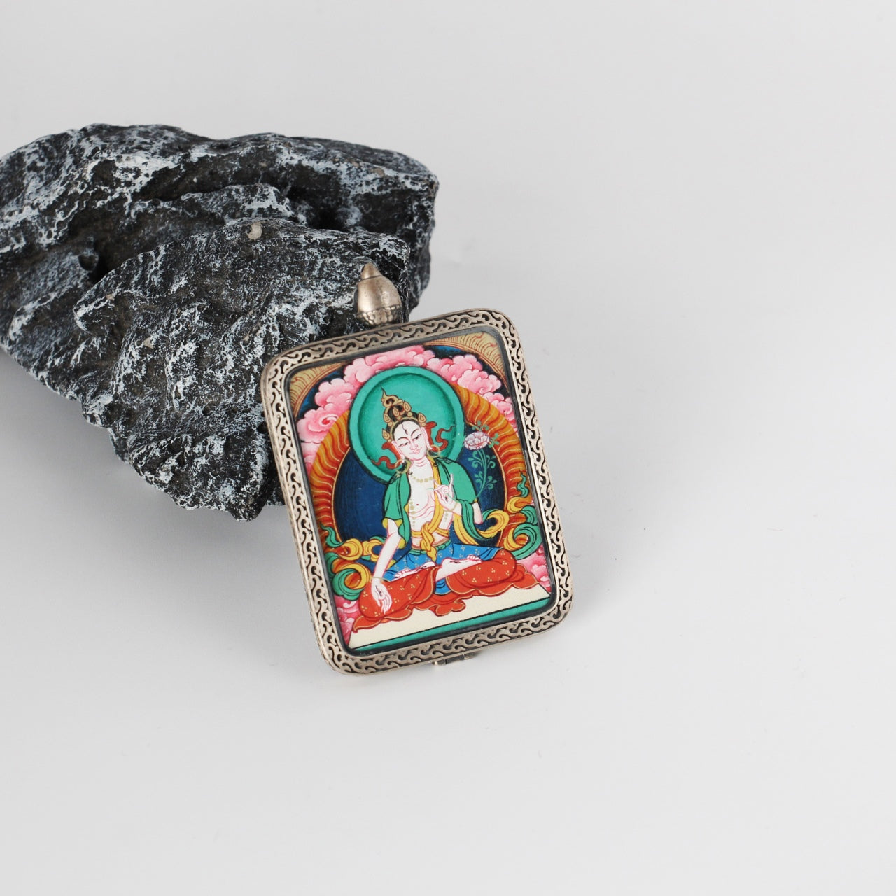White Tara mini Thangka pendant displayed on a stone prop, highlighting the vivid hand-painted artwork, turquoise-green halo, and ornate engraved silver border.