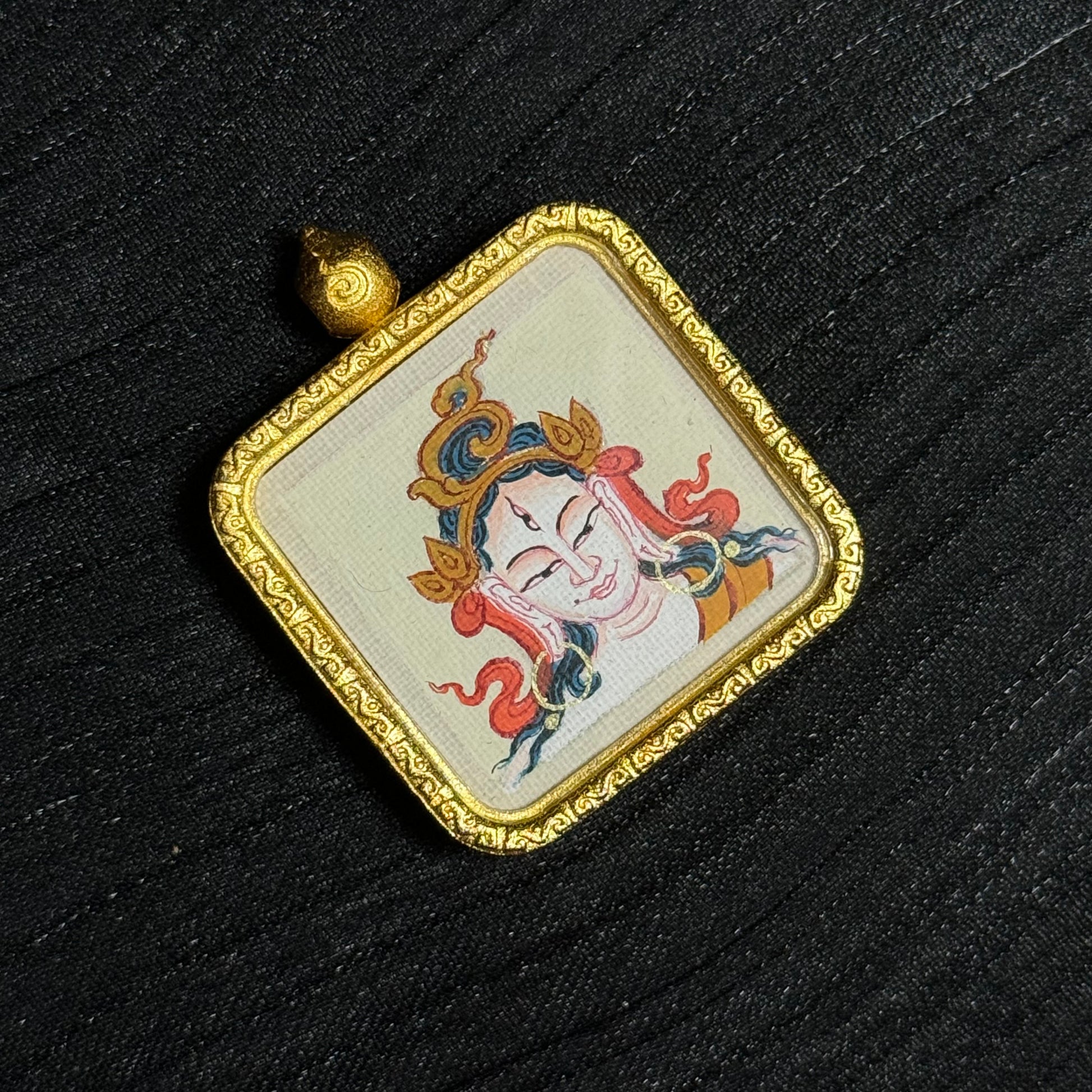 Detailed view of a White Tara miniature thangka pendant with traditional Tibetan deity painting, mounted in a square gold-toned frame with engraved decorative edge.