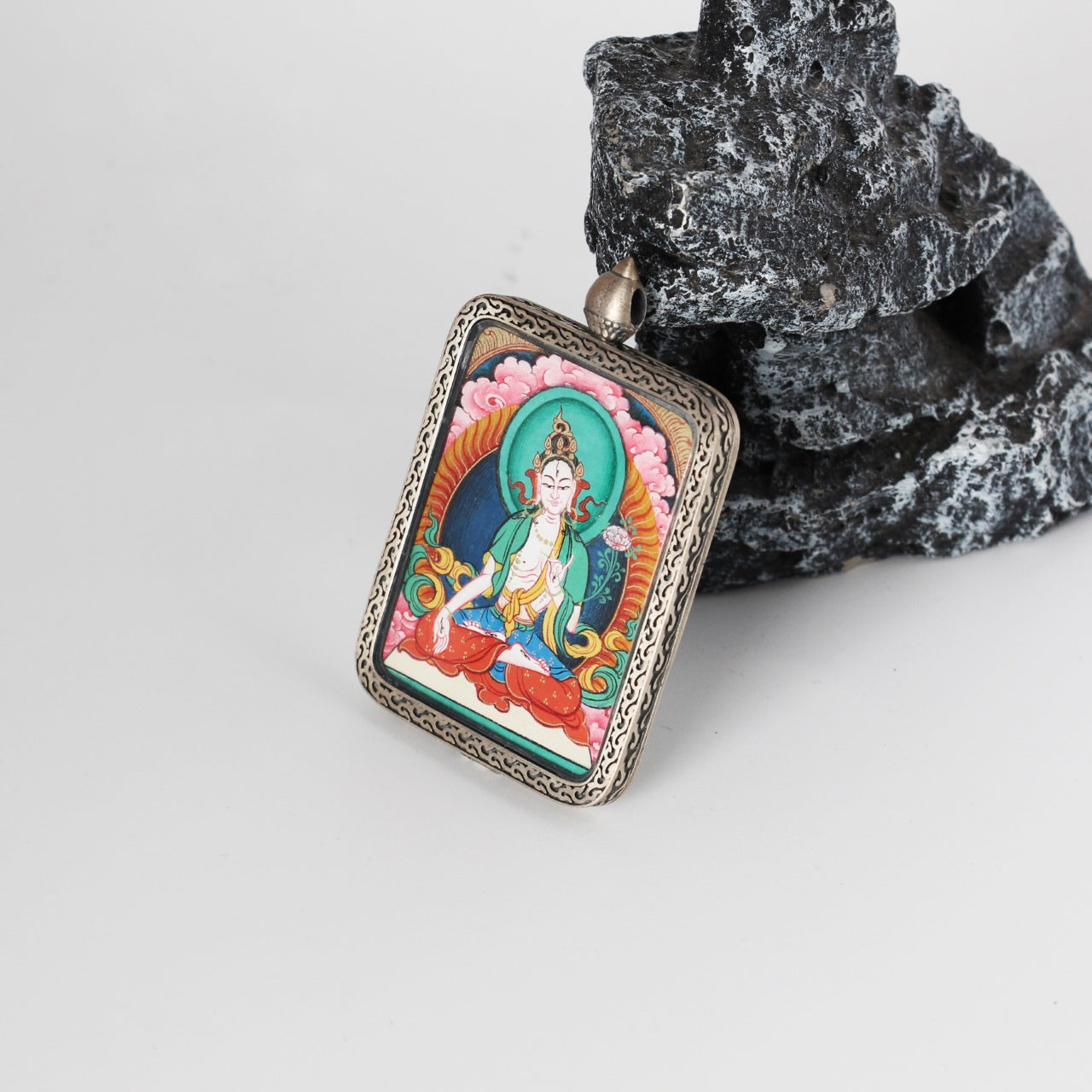 Angled view of White Tara mini Thangka pendant showing hand-painted deity details, mineral pigment color layering, and the engraved silver frame around the pendant.