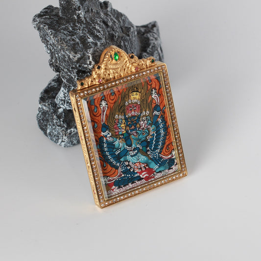 Angled view of the Yamantaka hand-painted mini thangka pendant showing the raised gold-tone frame, crystal-set border, and ornate top crown with green and red stone accents.