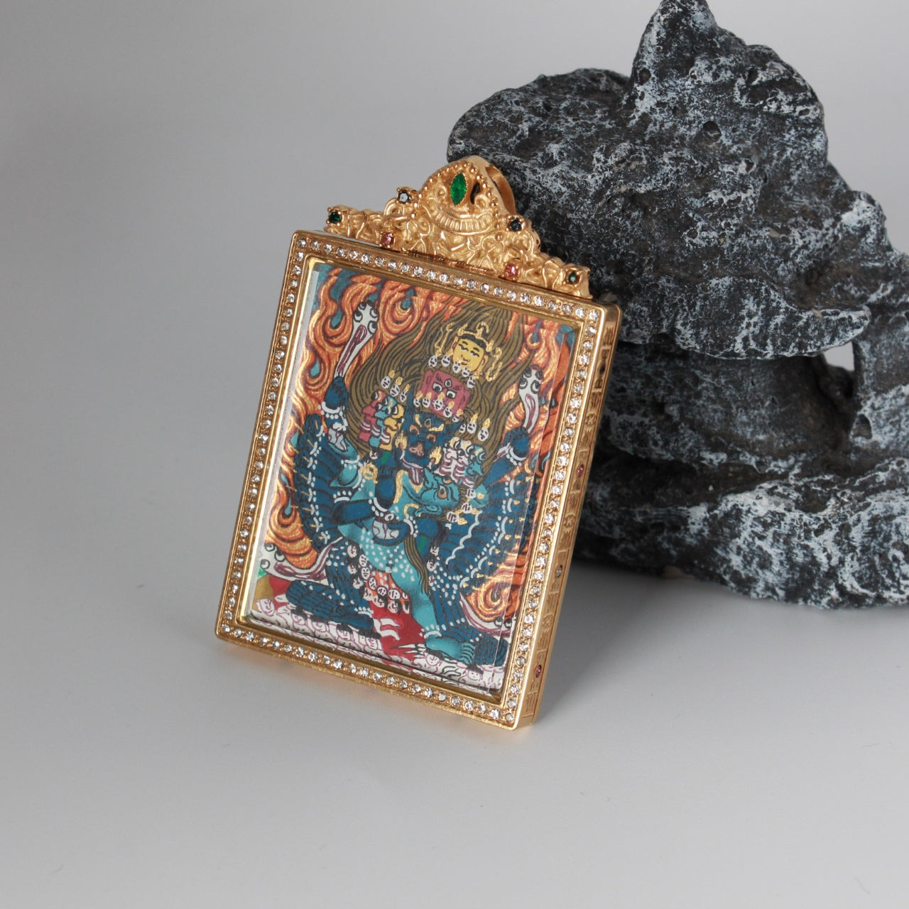 Side-angled view of the Yamantaka mini thangka pendant highlighting the thickness of the gold-tone titanium steel case, crystal-set perimeter, and clear protective cover over the painting.
