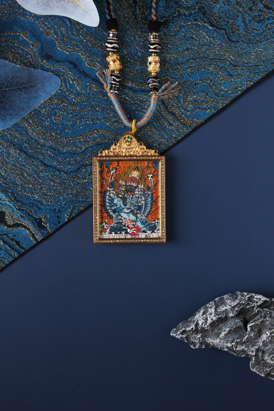 Yamantaka (Vajrabhairava) thangka pendant necklace in a double-sided jeweled titanium steel case, photographed on a blue textured background.