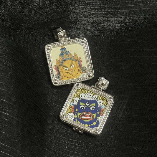 Two painted sides shown together: Yellow Jambhala face and wrathful Mahakala face, both on square mini thangka panels inside 925 silver electroplated gawu cases with beaded borders and corner studs