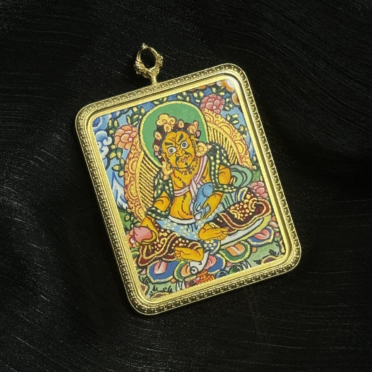 Detailed hand-painted Yellow Jambhala miniature thangka pendant artwork showing the Buddhist wealth guardian with traditional ornaments, lotus throne, and Himalayan decorative background.