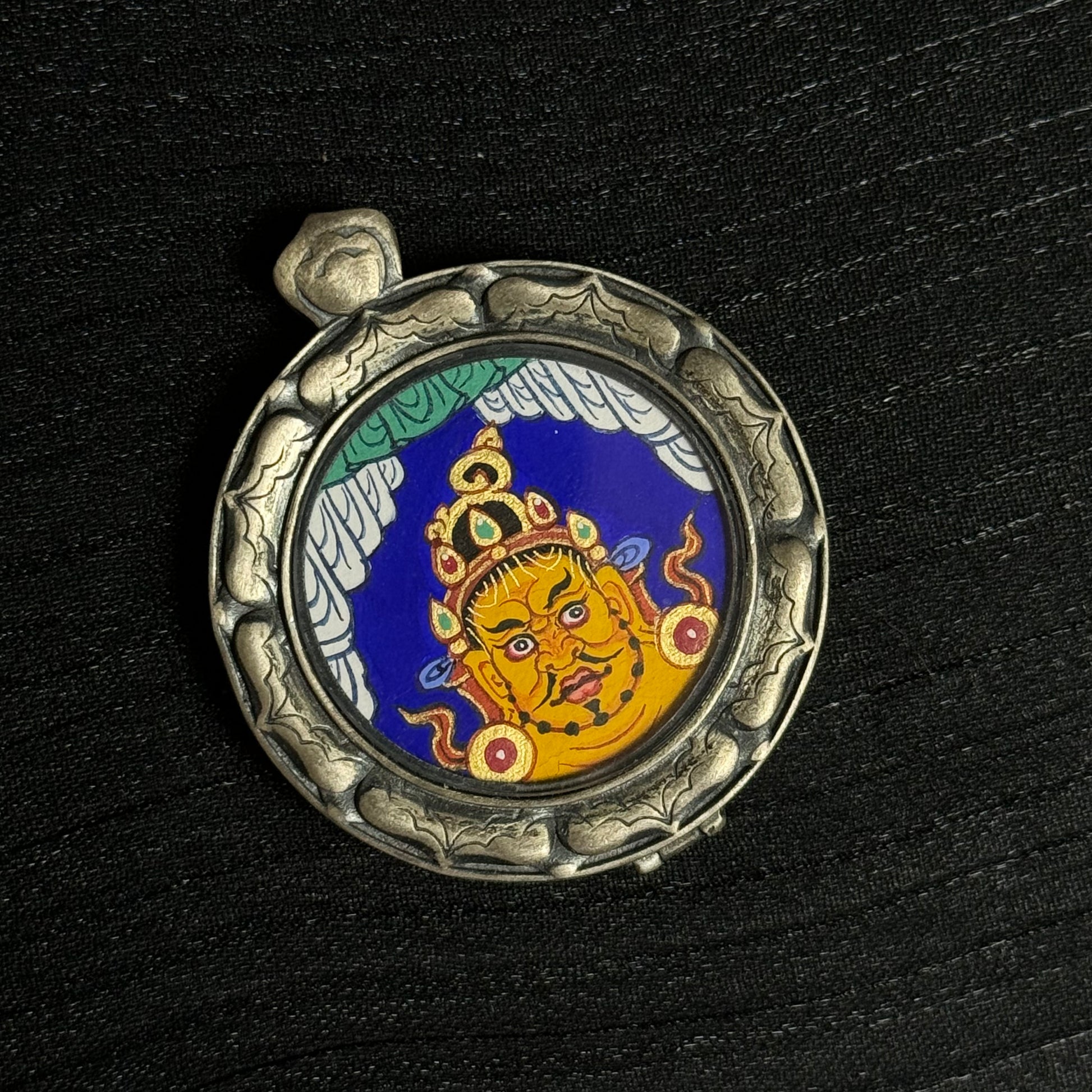 Detailed view of the Yellow Jambhala head mini thangka pendant showing the circular silver protective frame and the hand-painted deity portrait.
