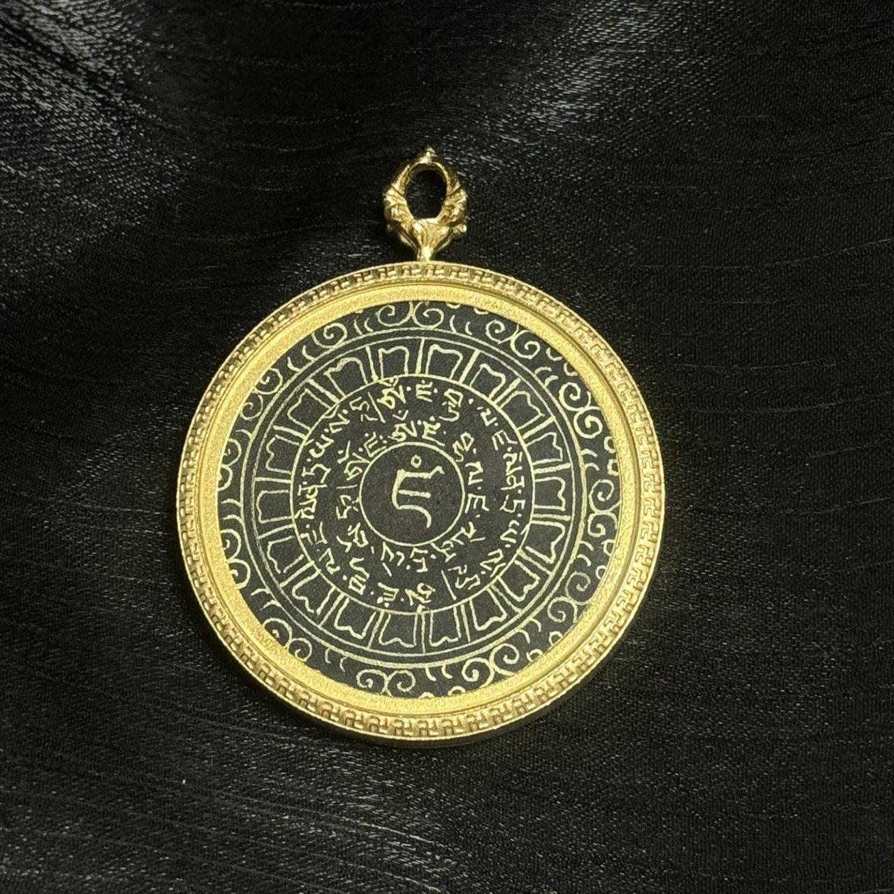 Close view of the Yellow Jambhala heart mantra pendant showing the gold-tone rim texture, decorative outer border, and metal hanging loop connection at the top.