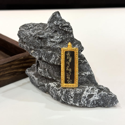 Upright view of Yellow Jambhala mantra mini thangka pendant, showing Tibetan script on a black background, framed by an ornate gold-toned copper case.