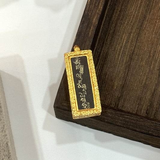 Angled view of the Yellow Jambhala mantra pendant, highlighting the raised decorative pattern on the gold-toned copper frame and the pendant bail detail.