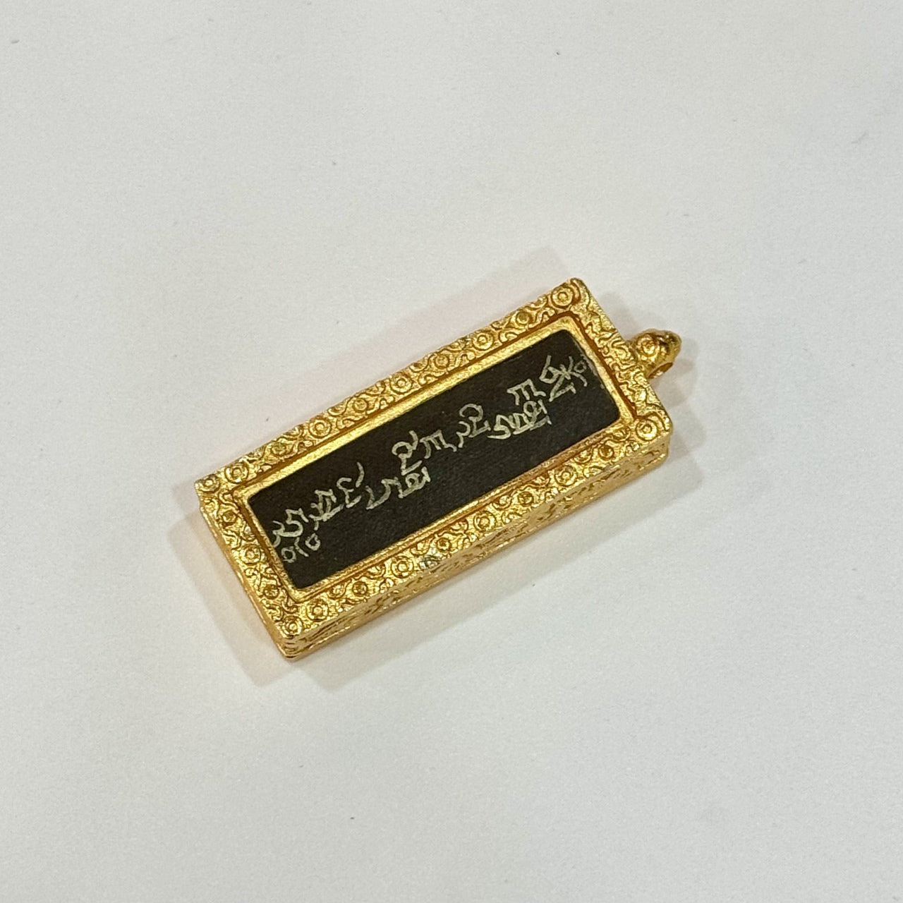 Flat lay of Yellow Jambhala mantra pendant, focusing on the Tibetan script lettering, black background contrast, and ornate gold-toned copper border.