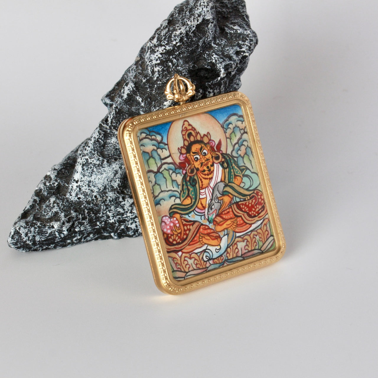 Angled front view of Yellow Jambhala pendant highlighting the gold-tone titanium steel frame, patterned border, and vajra-style bail above the hand-painted thangka image.