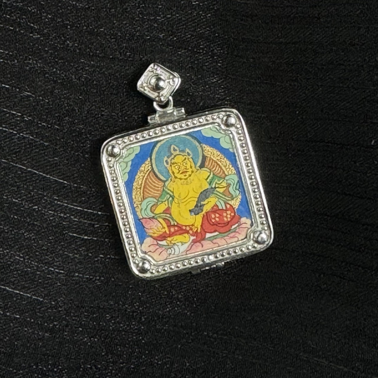 Angled view of Yellow Jambhala pendant showing raised silver case profile, square bail detail, and crisp hand-painted mineral pigment lines