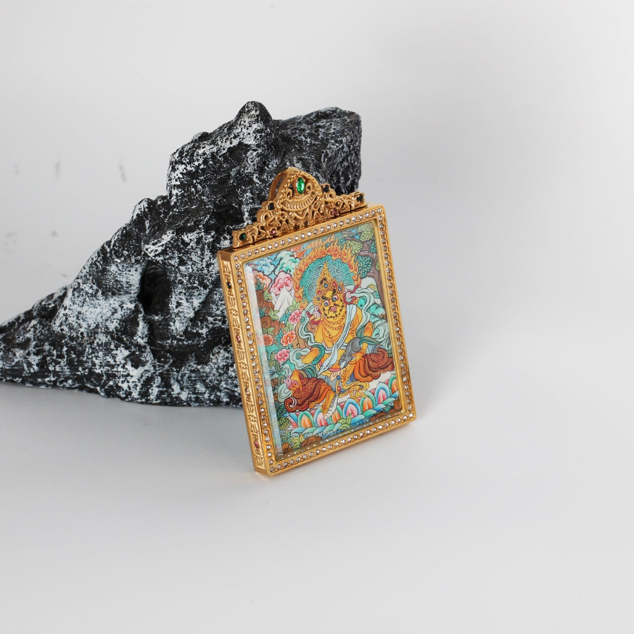 Angled view of Yellow Jambhala mini thangka pendant showing the thickness and structure of the titanium steel case, with finely detailed hand-painted Nepalese thangka artwork visible inside