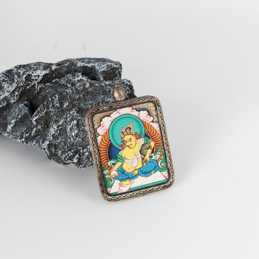 Angled view of Yellow Jambhala mini thangka pendant highlighting the textured sterling silver frame, raised border pattern, and layered mineral pigment colors on the painting