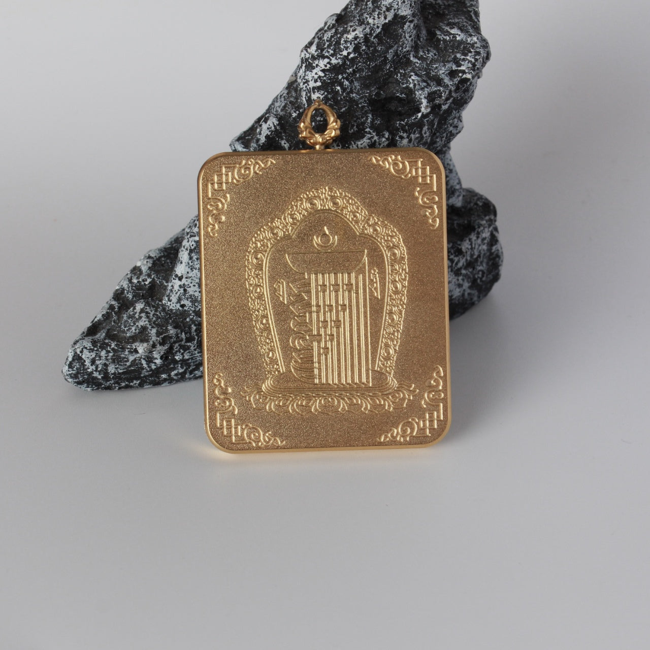 Back view of Yellow Jambhala mini thangka pendant featuring an embossed central motif with decorative corner patterns on a matte-textured gold-tone titanium steel case.