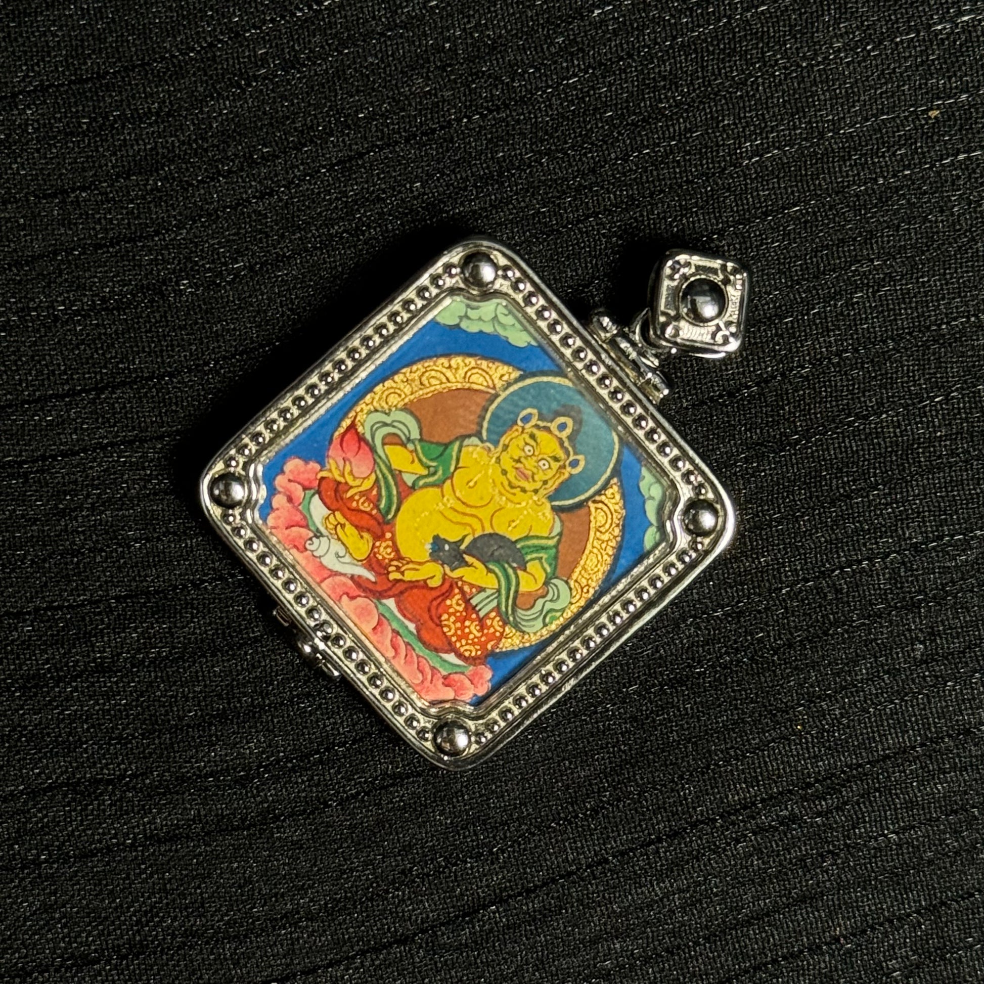 Close angled detail of Yellow Jambhala thangka pendant highlighting vivid mineral pigment layers and Tibetan Buddhist iconography