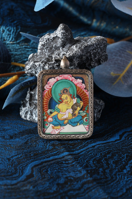 Close-up product photo of the Yellow Jambhala mini thangka pendant highlighting hand-painted mineral pigment craftsmanship and the sterling silver protective case, designed for collectors and practitioners seeking a durable portable thangka piece.