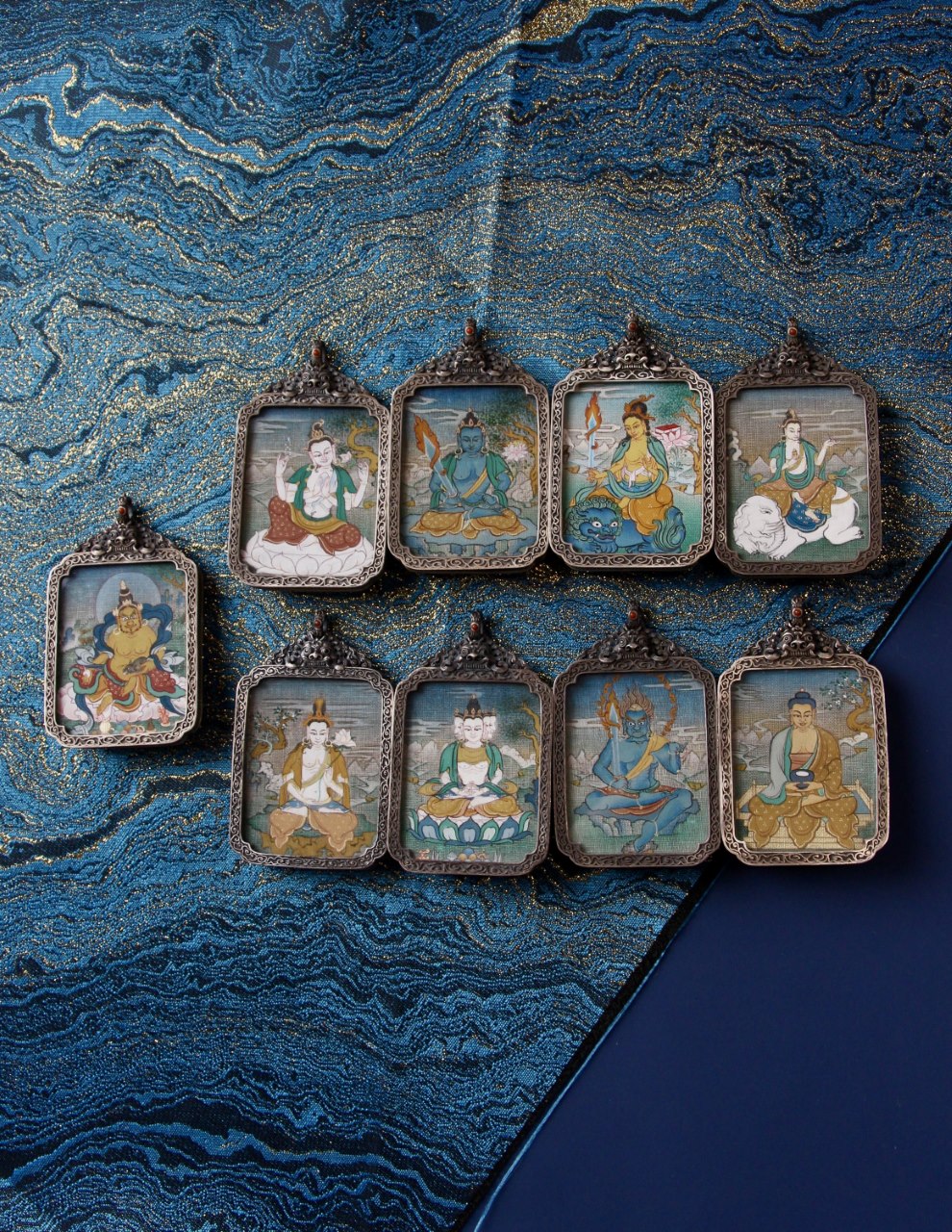 Collection display of Yellow Jambhala (Jambhala) mini thangka pendants arranged on blue brocade; each piece is hand-painted with mineral pigments and set in a vintage-style silver gawu case, painting size 3.5 × 4.5 cm—an iconography traditionally associated with generosity, prosperity aspirations, and steady accumulation (often resonating with Taurus/Virgo/Capricorn meanings of stability and disciplined growth).

中文翻译：