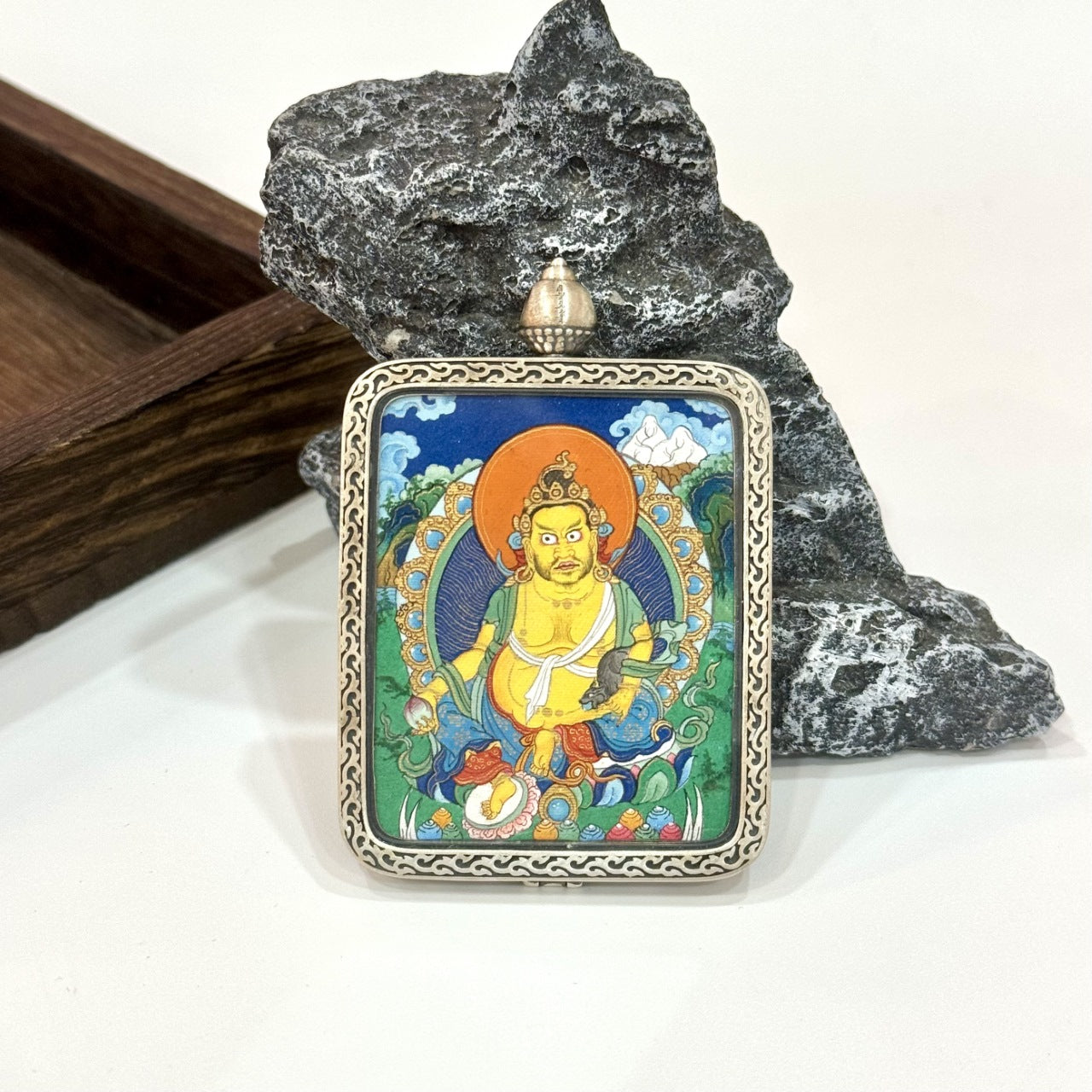 Yellow Jambhala mini thangka pendant displayed upright, featuring a Dunhuang Nine-Color Deer silver case, ornate border pattern, and detailed mineral pigment painting.