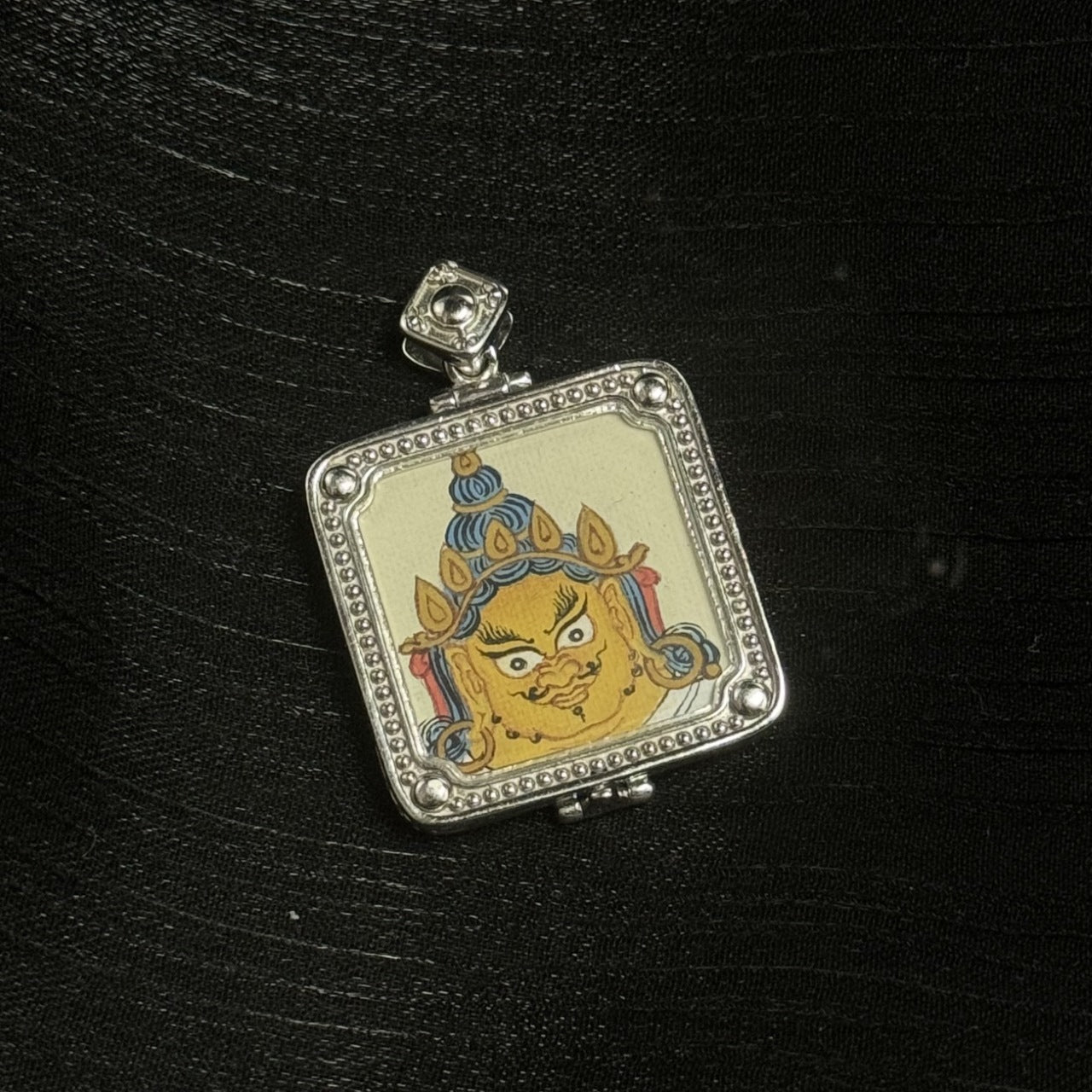 Close-up of Yellow Jambhala face painting with crown and blue hair detail, set in a square 925 silver electroplated gawu case with beaded edging and corner studs