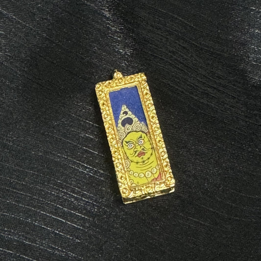 Front view of a Yellow Jambhala mini thangka pendant featuring a hand-painted yellow face with strong expression lines, white-and-gold crown patterns, deep blue background, and an ornate raised border around the copper case frame.