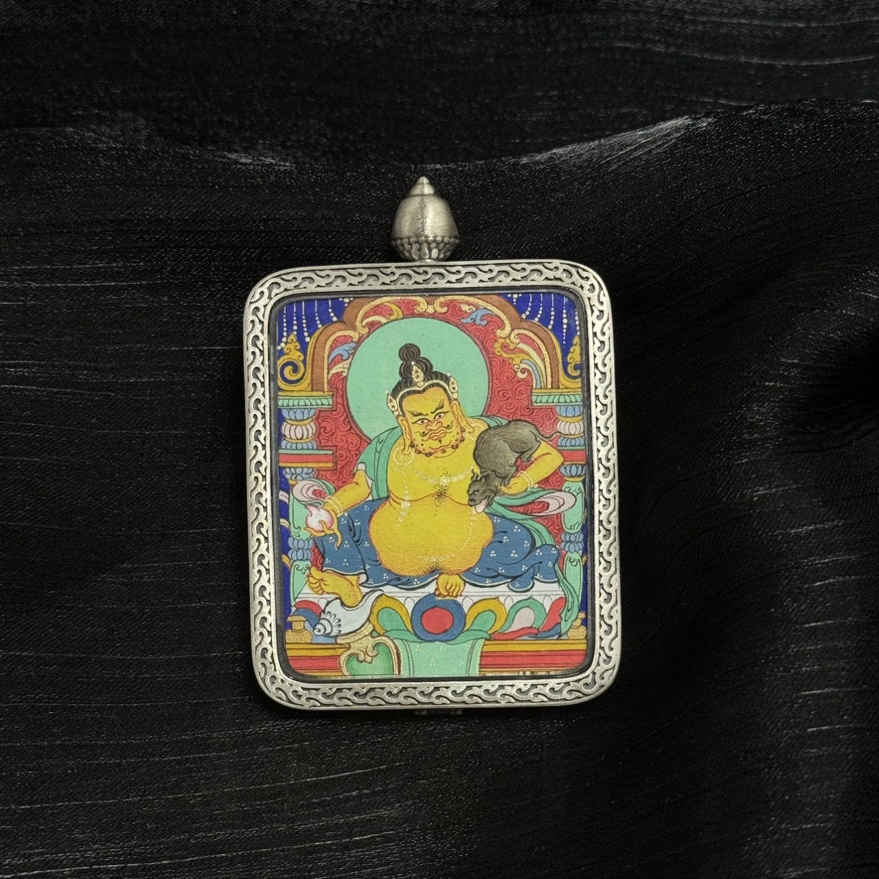 Front view of Yellow Jambhala mini thangka pendant, hand-painted with mineral pigments, featuring detailed Tibetan iconography and housed in a Dunhuang Nine-Color Deer silver gawu case.
