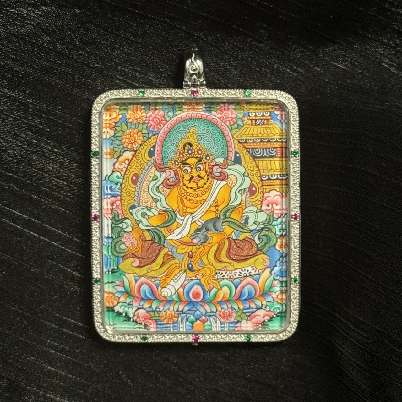 Detailed close-up of a Yellow Jambhala mini thangka pendant highlighting the lotus pedestal, halo decoration, jewelry ornaments, and mineral pigment painting details.