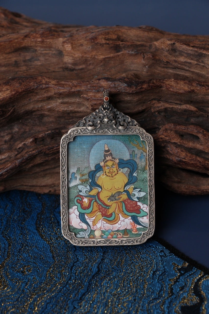 Yellow Jambhala mini thangka pendant in a vintage silver gawu case displayed on blue brocade; mineral pigment hand-painting, 3.5 × 4.5 cm—evoking auspicious abundance themes and forward-moving opportunity (often resonating with Sagittarius-style optimism).