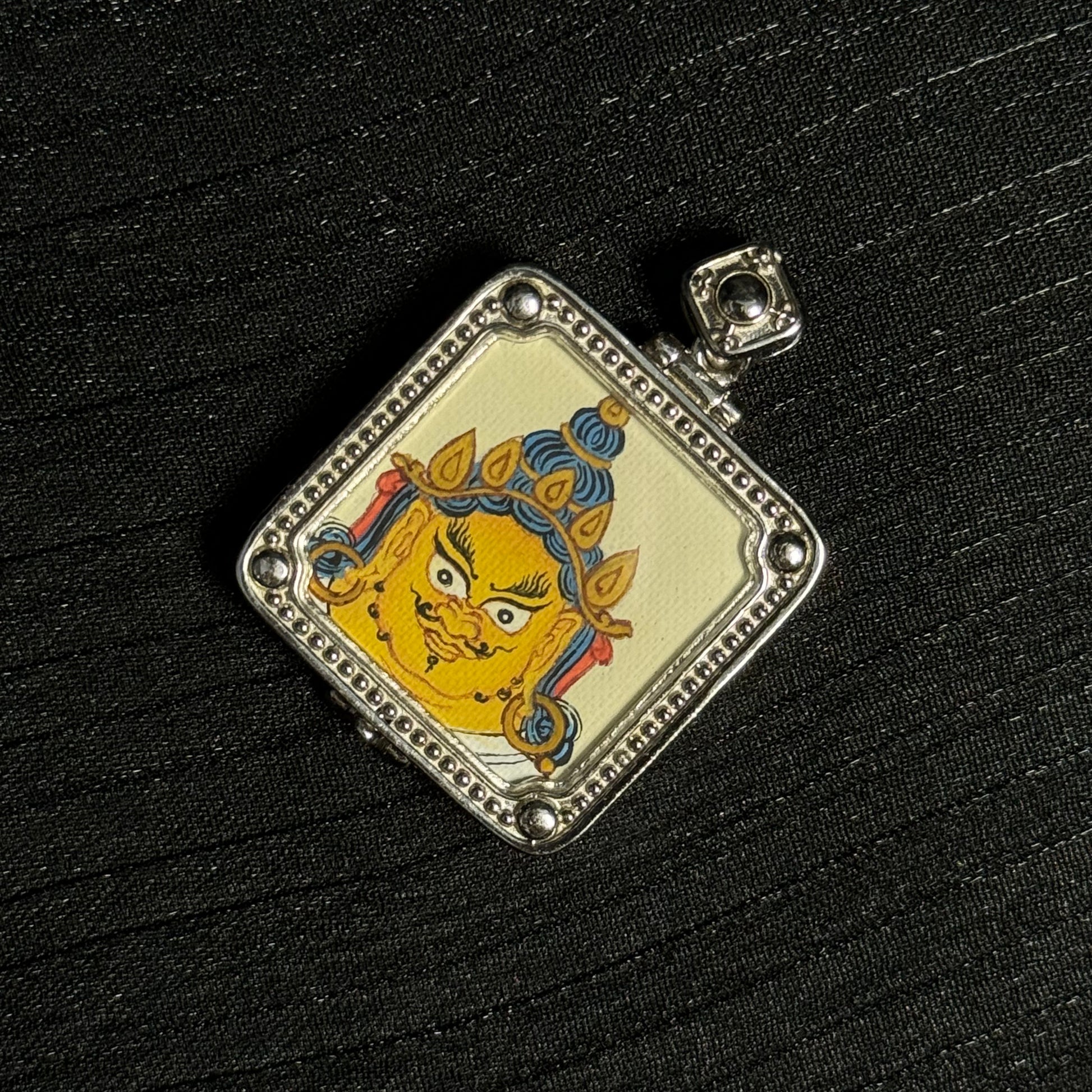 Top angled view of Yellow Jambhala mini thangka pendant showing Tibetan gawu style case and miniature thangka painting