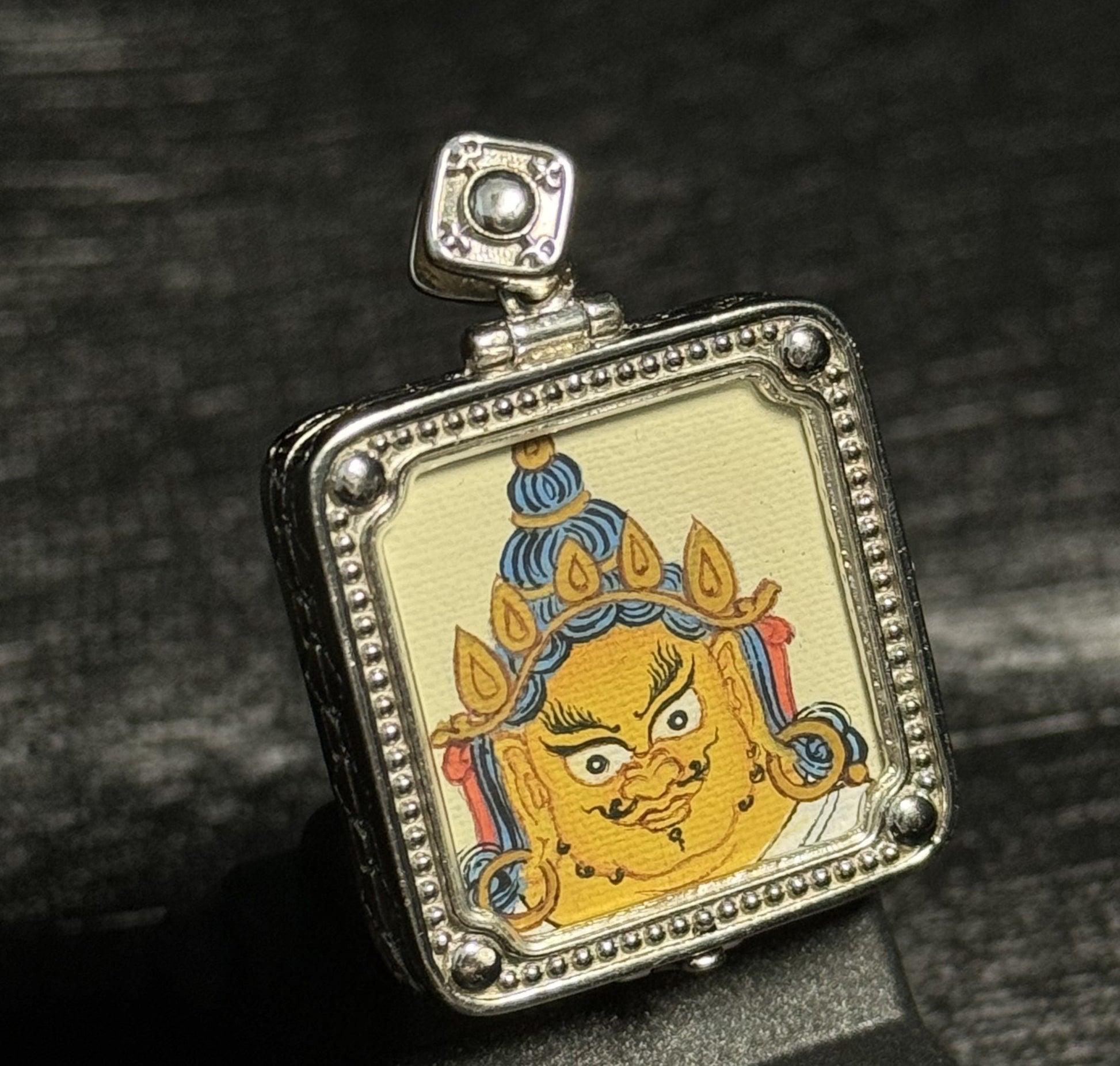 Close angled view of Yellow Jambhala thangka pendant highlighting Tibetan miniature painting and vibrant mineral pigment layers