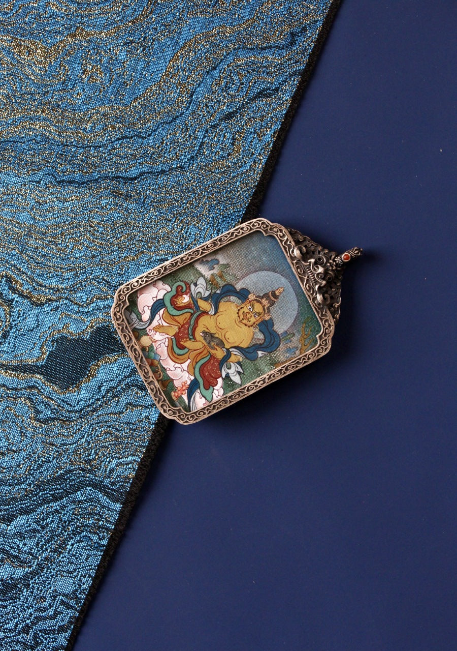 Close-up of Yellow Jambhala (Jambhala) mini thangka pendant in a vintage silver gawu case; vivid colors and fine detailing created with mineral pigments, 3.5 × 4.5 cm—an iconography associated with generosity, abundance aspirations, and confident momentum (often linked with Leo-style positivity).
