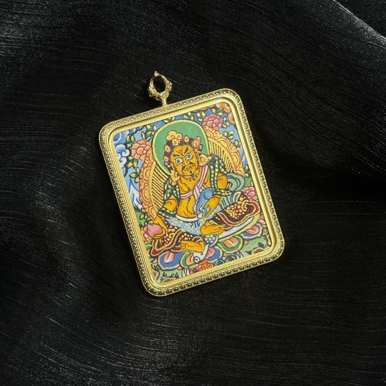 Portable mini thangka pendant depicting Yellow Jambhala seated in a traditional Buddhist iconographic posture with lotus base and decorative floral background in Nepal thangka painting style.