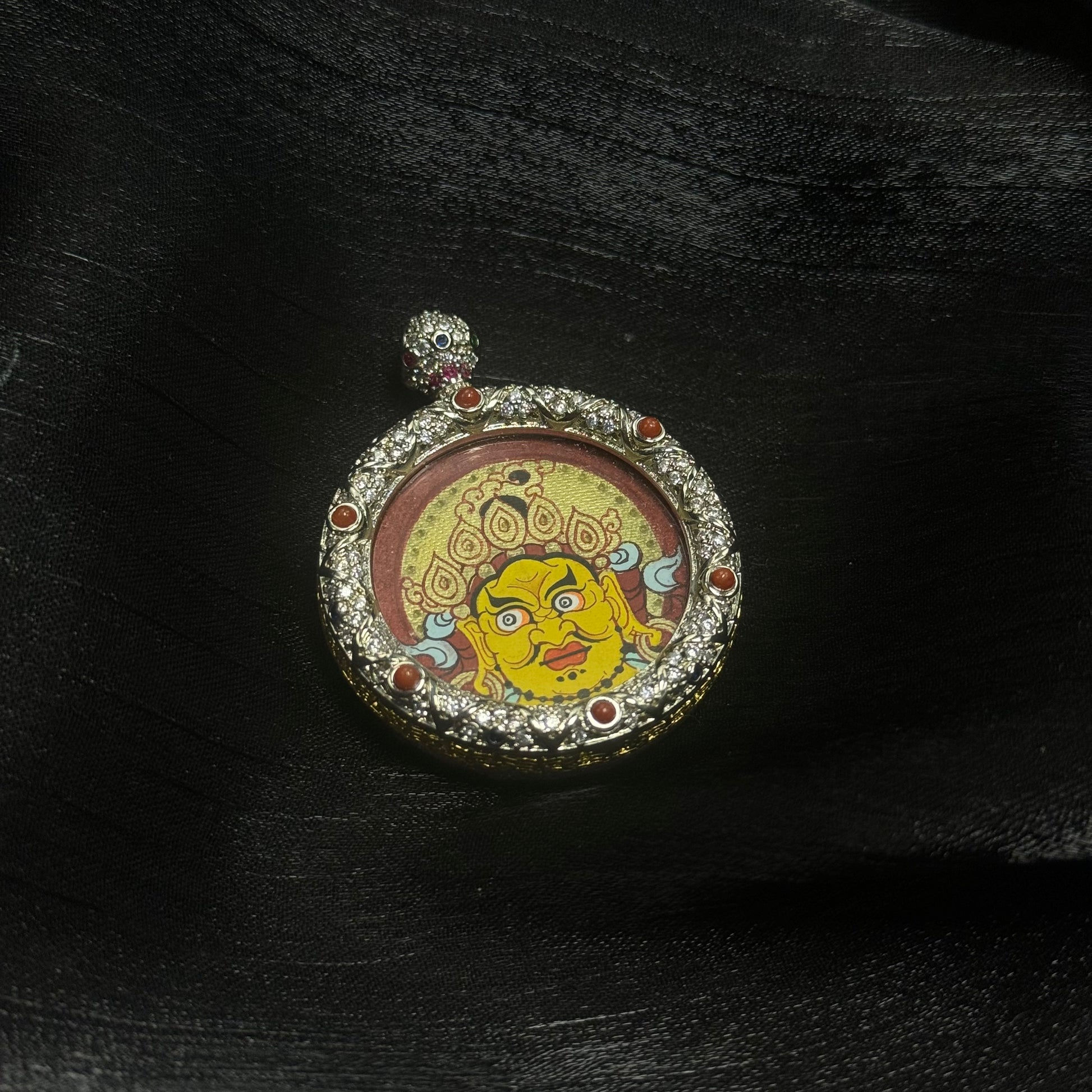 Close-up detail of Yellow Jambhala thangka painting with layered mineral pigments, gold decorative halo motifs, and a circular jewelry-style copper pendant setting.