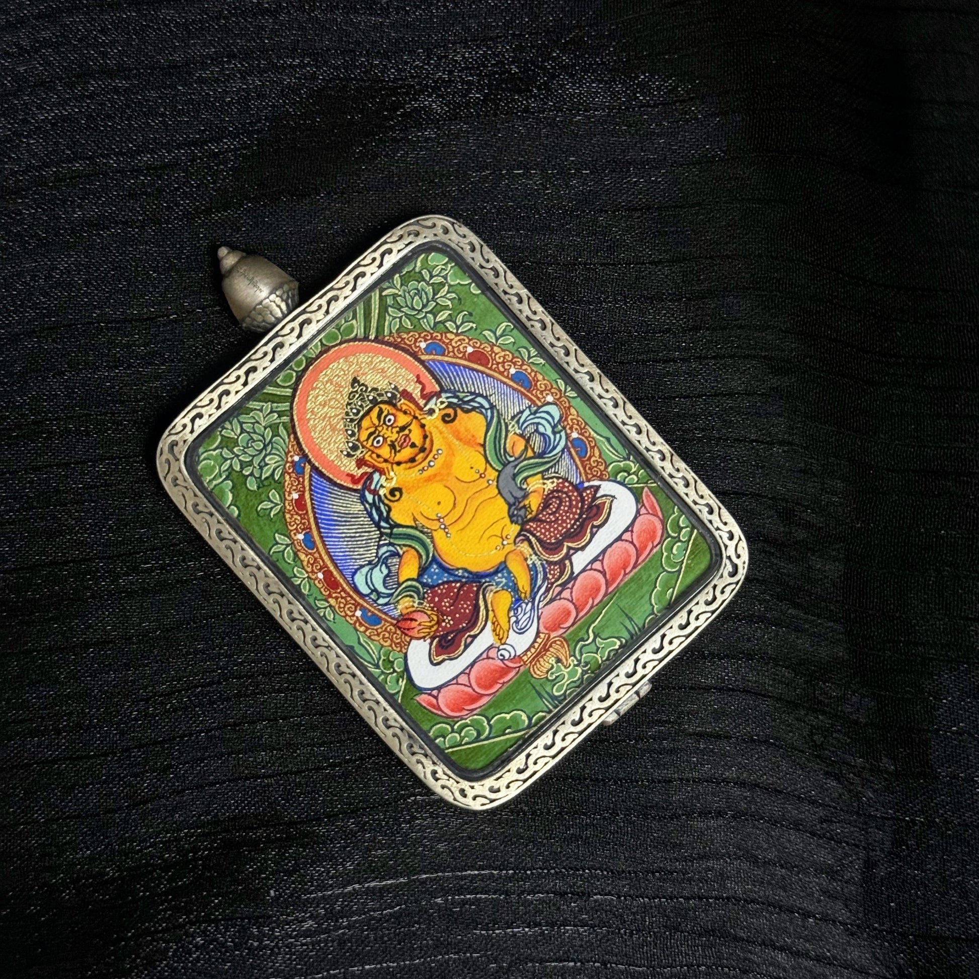 Top view of Yellow Jambhala mini thangka pendant in Rebgong style, hand-painted with mineral pigments and set inside a detailed 925 silver pendant frame