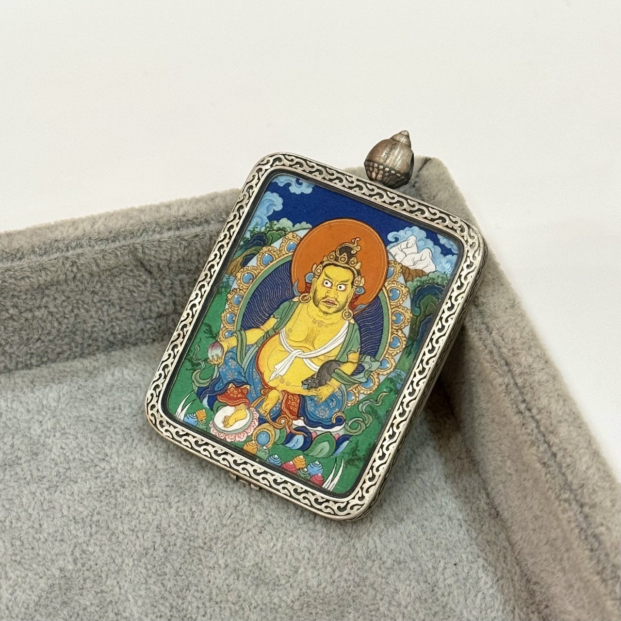 Angled view of Yellow Jambhala thangka pendant, highlighting the textured silver frame, raised edge detailing, and the vivid hand-painted deity artwork.