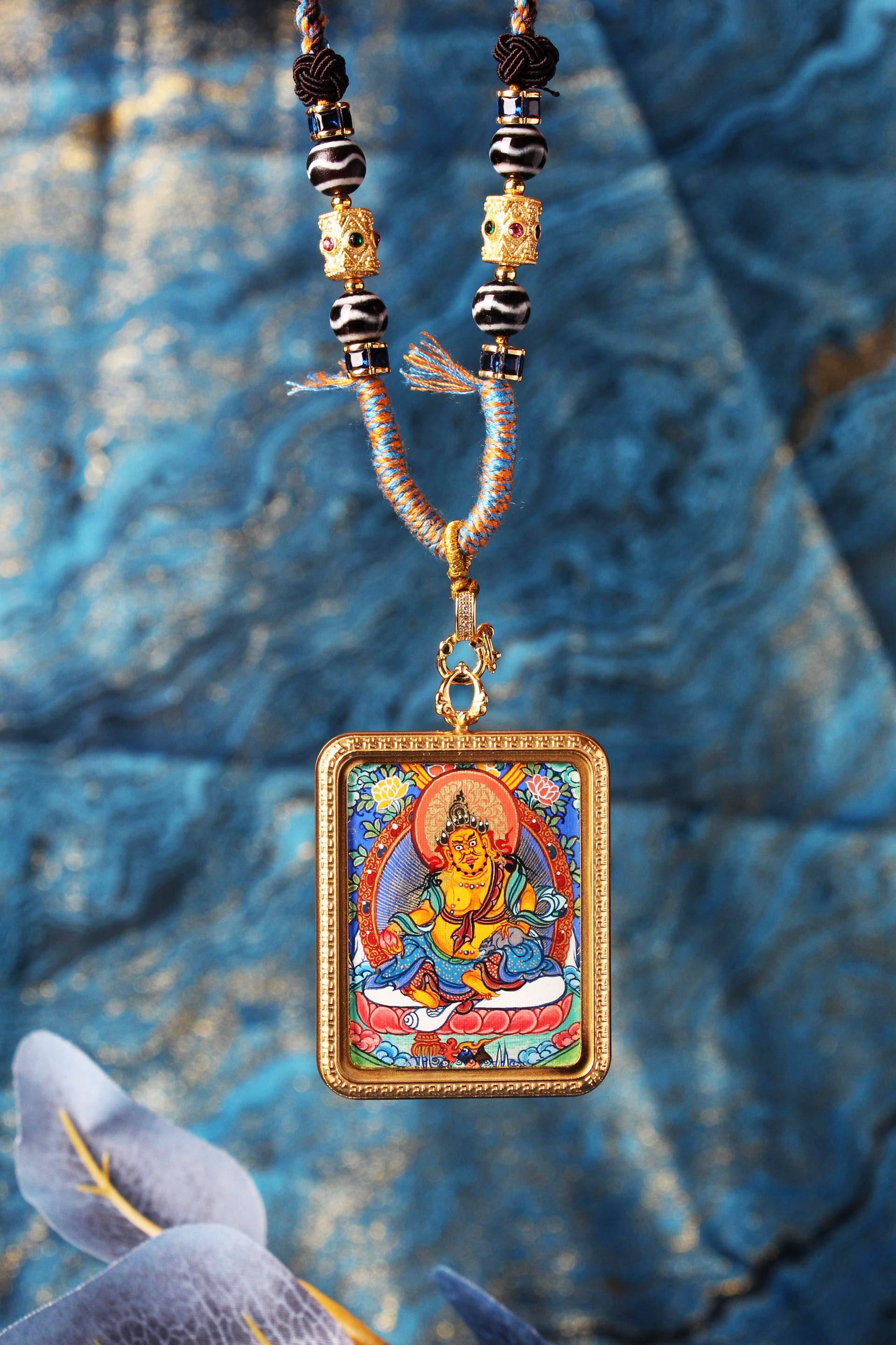 Close-up of Yellow Jambhala mini thangka pendant showing detailed mineral pigment painting of Dzambhala, ornate halo, lotus seat, and handcrafted beadwork on the necklace.