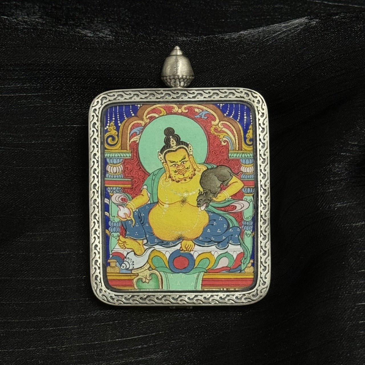 Full view of Yellow Jambhala thangka pendant presented in a Dunhuang Nine-Color Deer silver gawu case, showing complete painting layout and protective metal craftsmanship.