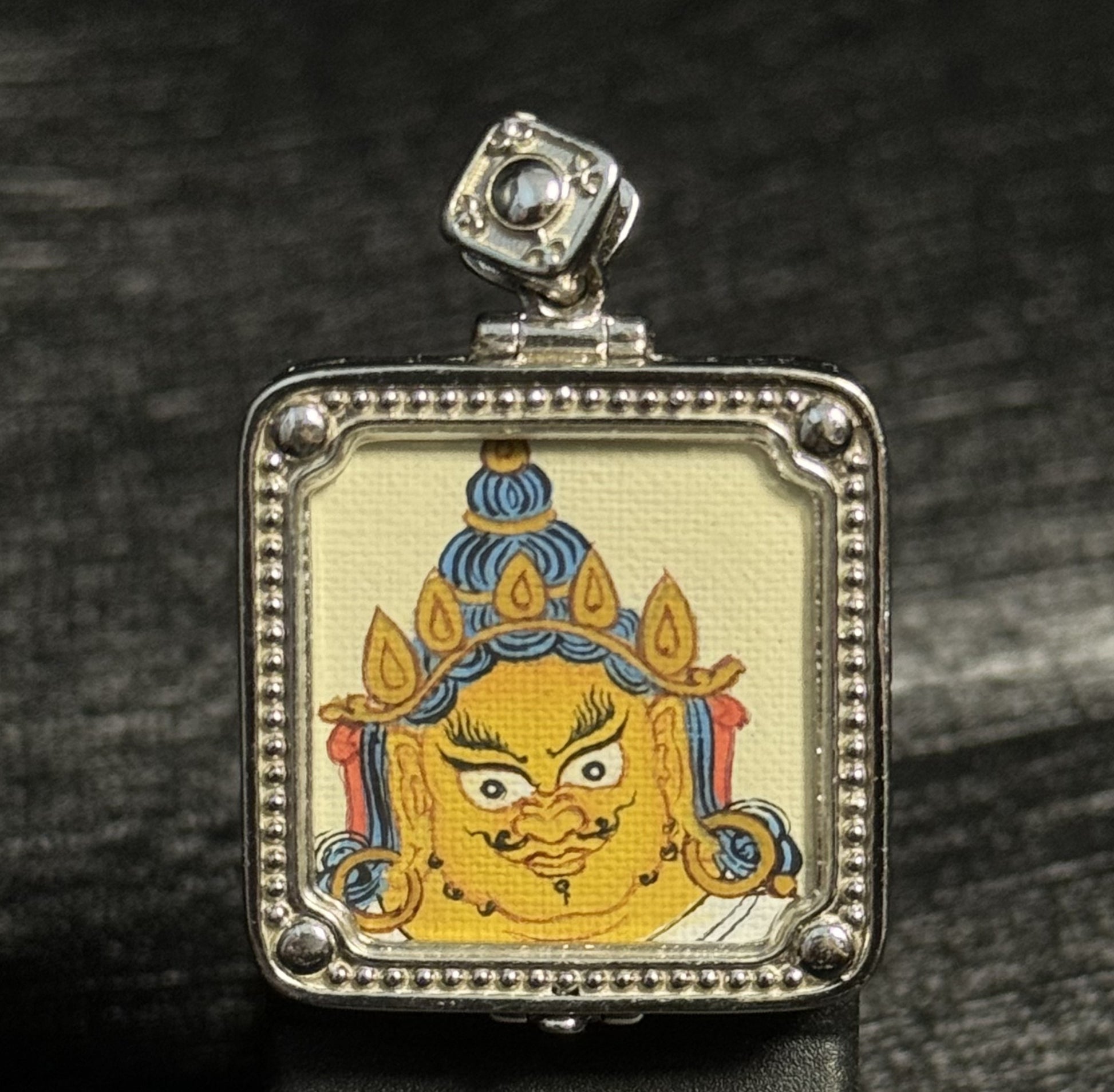 Front view of Yellow Jambhala mini thangka pendant featuring hand-painted Tibetan thangka art with natural mineral pigments in a silver gawu pendant frame