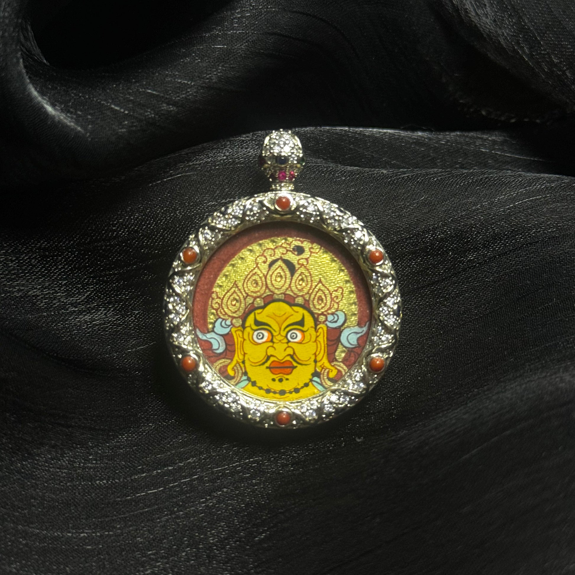 Macro view of Yellow Jambhala mini thangka pendant highlighting the gemstone-decorated copper frame, hand-painted deity portrait, and rich red-gold color composition.